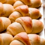 Side view of homemade Crescent rolls lined up on a baking sheet.