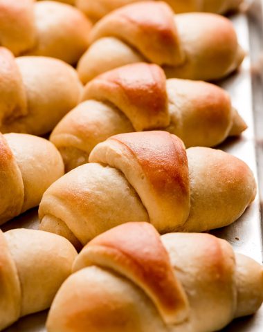 Side view of homemade Crescent rolls lined up on a baking sheet.
