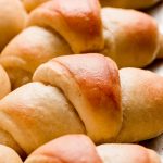 Side view of homemade Crescent rolls lined up on a baking sheet.