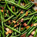 Green Beans Almondine in a skillet with a wooden spoon and lemon halves to the side.
