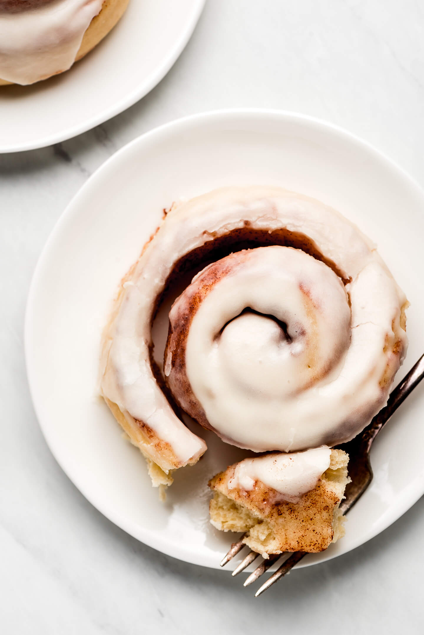 Frosted Cinnamon Roll partially unwound with a piece cut off and on a fork.