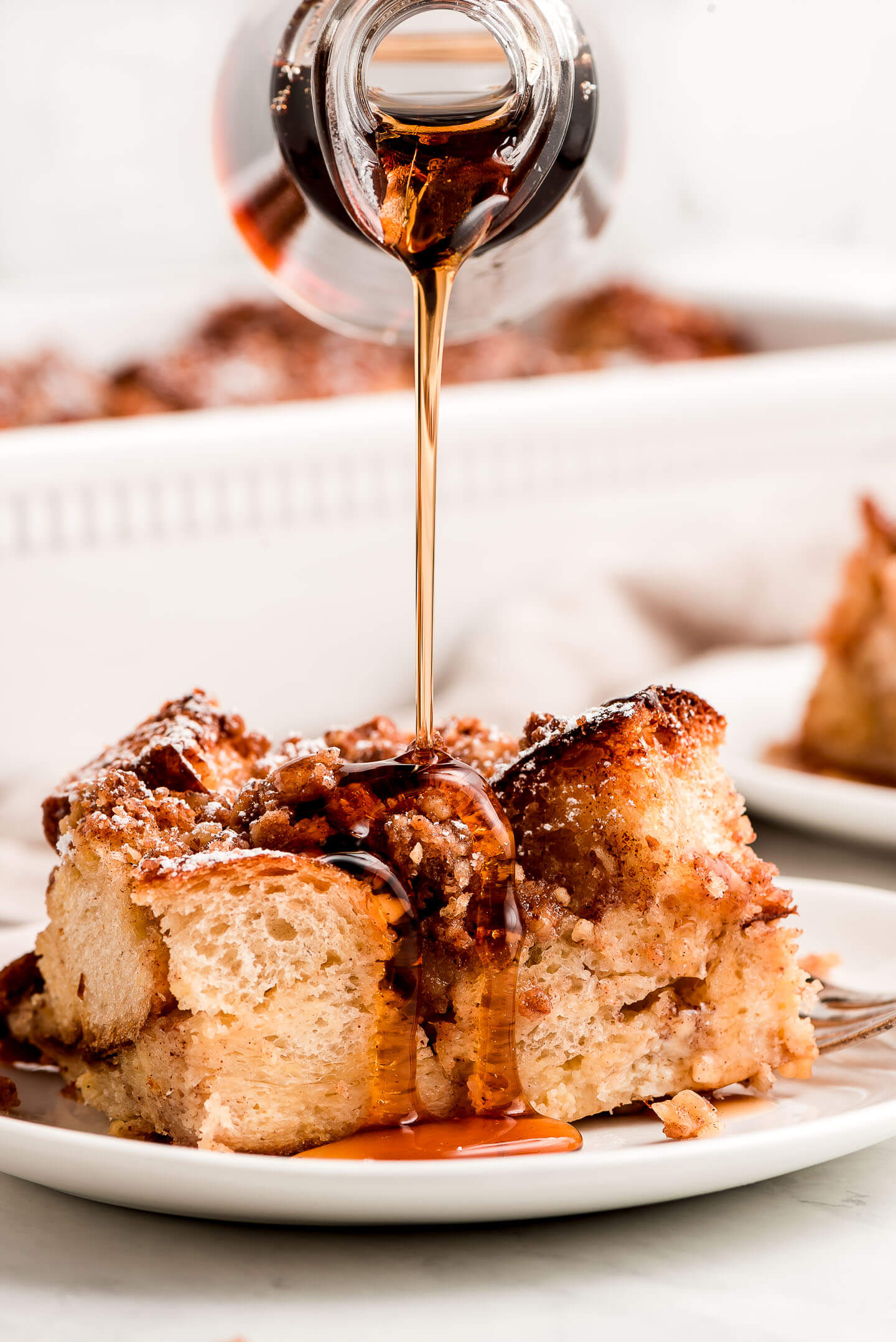 Maple syrup streaming down out of a bottle onto a slice of French Toast Casserole.