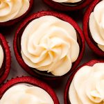 Close up of the top of red cupcakes topped with ganache and cream cheese frosting.