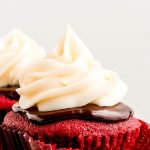 Close up of a Red Velvet cupcake topped with ganache and cream cheese frosting on a pink platter.