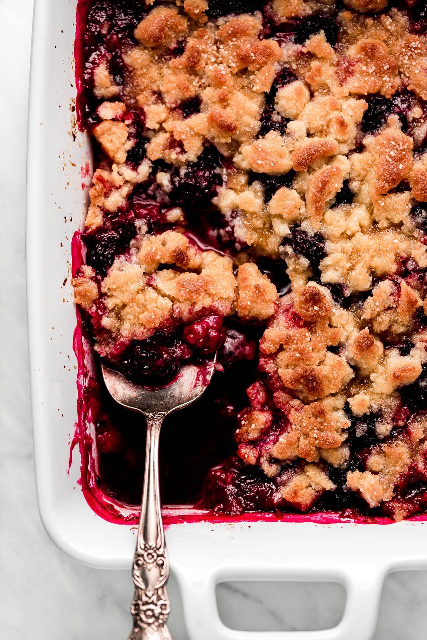 A white casserole dish of Blackberry Cobbler with a serving spoon scooping some out.