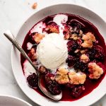 Blackberry Cobbler in a bowl topped with ice cream that is starting to melt.