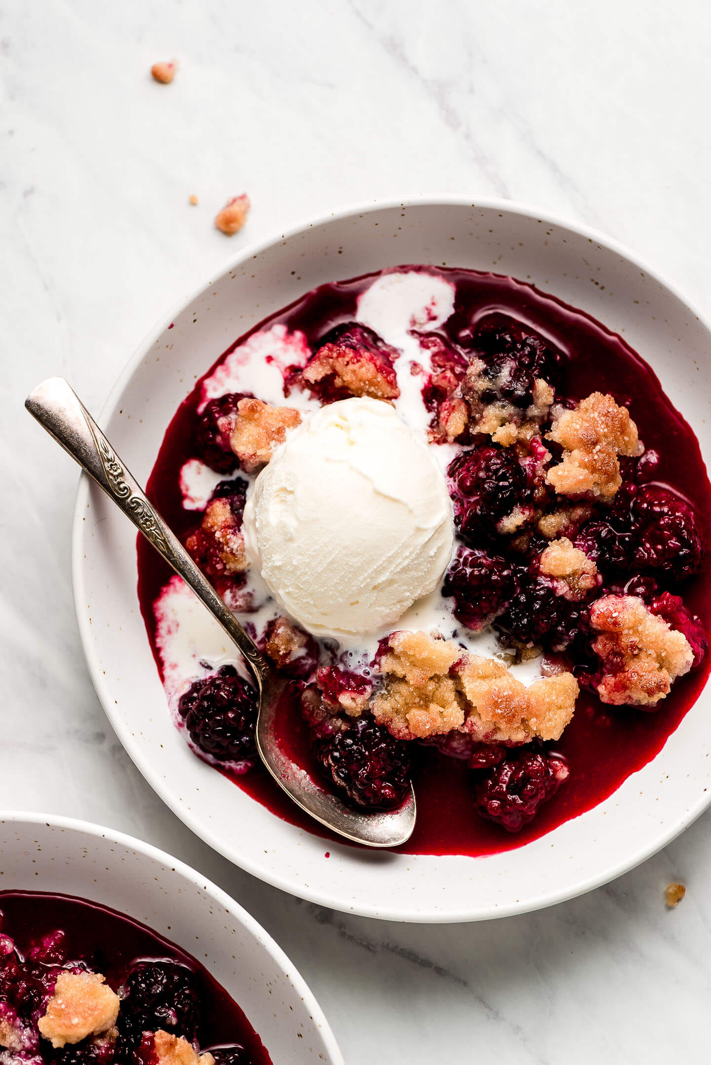 Blackberry Cobbler in a bowl topped with ice cream that is starting to melt.