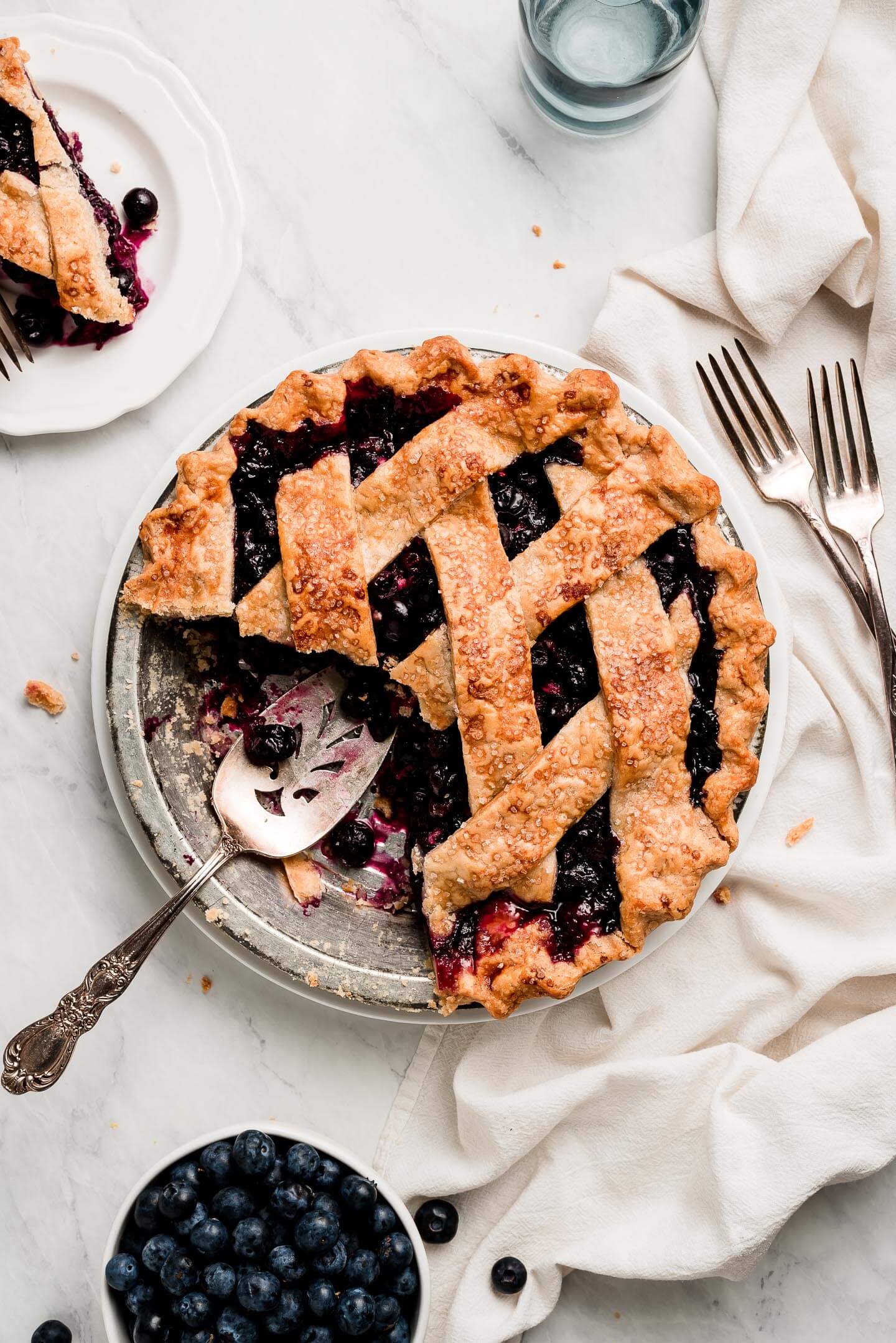 Lattice Blueberry Pie with a slice to the side and a bowl of blueberries.