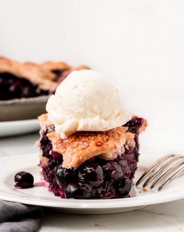 A slice of Homemade Blueberry Pie with a scoop of ice cream on top.