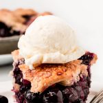 A slice of Homemade Blueberry Pie with a scoop of ice cream on top.