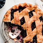 Blueberry Pie with a few pieces gone, a piece on a plate, and bowl of blueberries.
