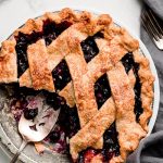 Lattice Blueberry Pie with a slice to the side and a bowl of blueberries.