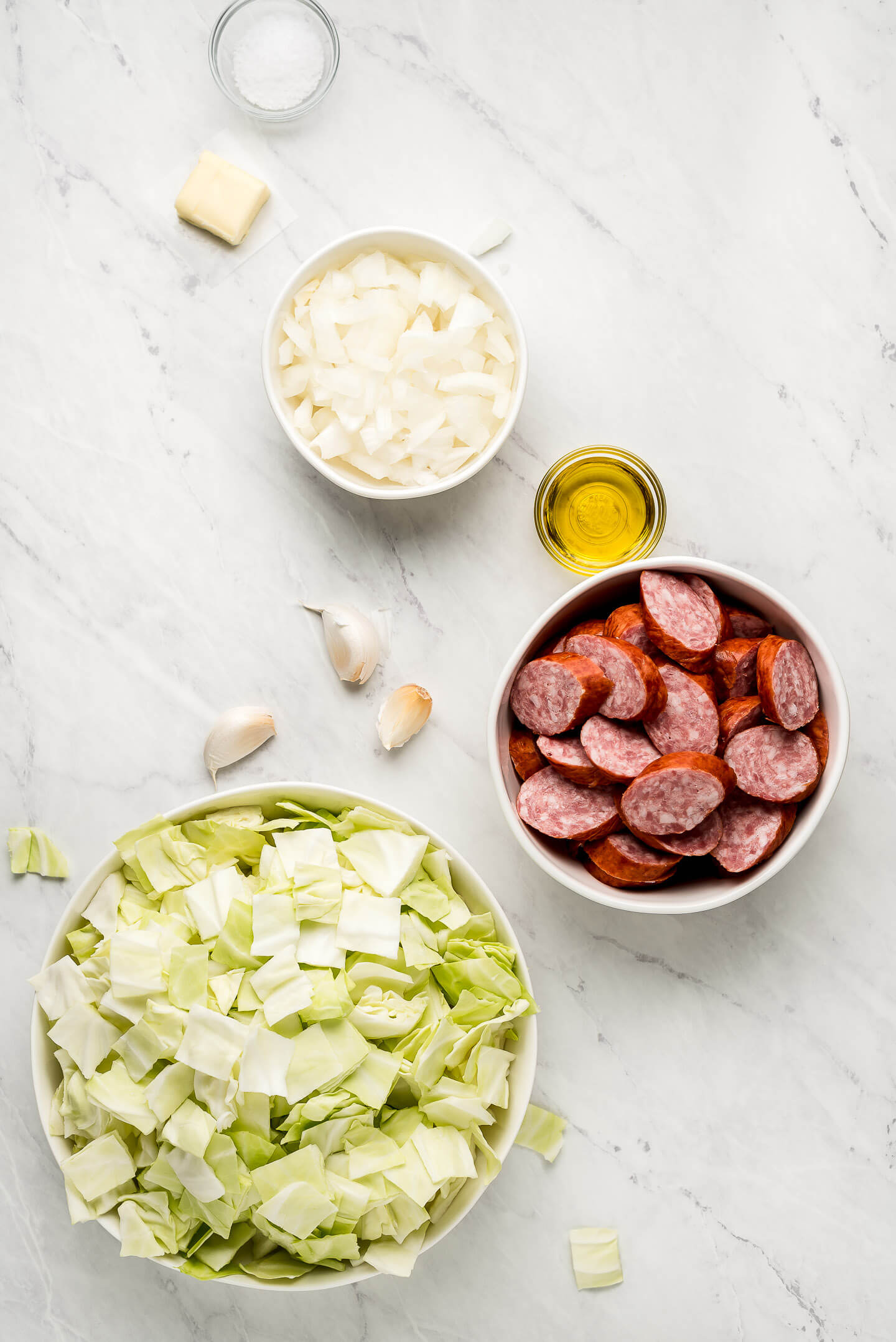 Ingredients on a marble surface- onions, butter, oil, sausage, garlic, and cabbage.