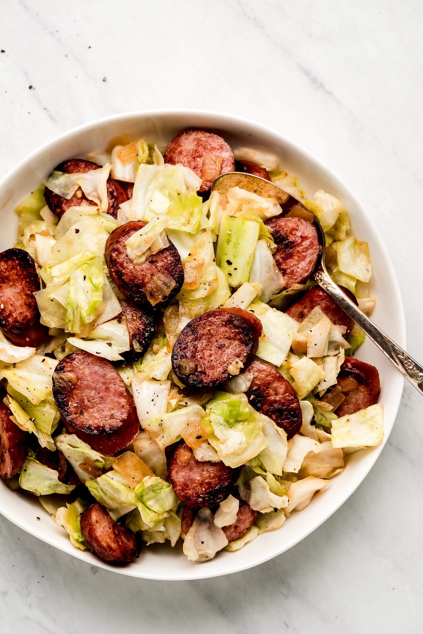 Cabbage and Sausage in a large white bowl with a spoon in the side.