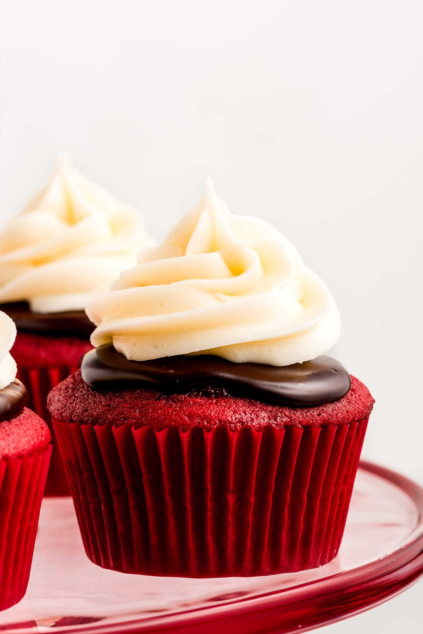 Close up shot of a Red Velvet Cupcake topped with dark chocolate ganache and a swirl of Cream Cheese Frosting.