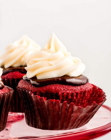 Close up of a Red Velvet cupcake topped with ganache and cream cheese frosting on a pink platter.