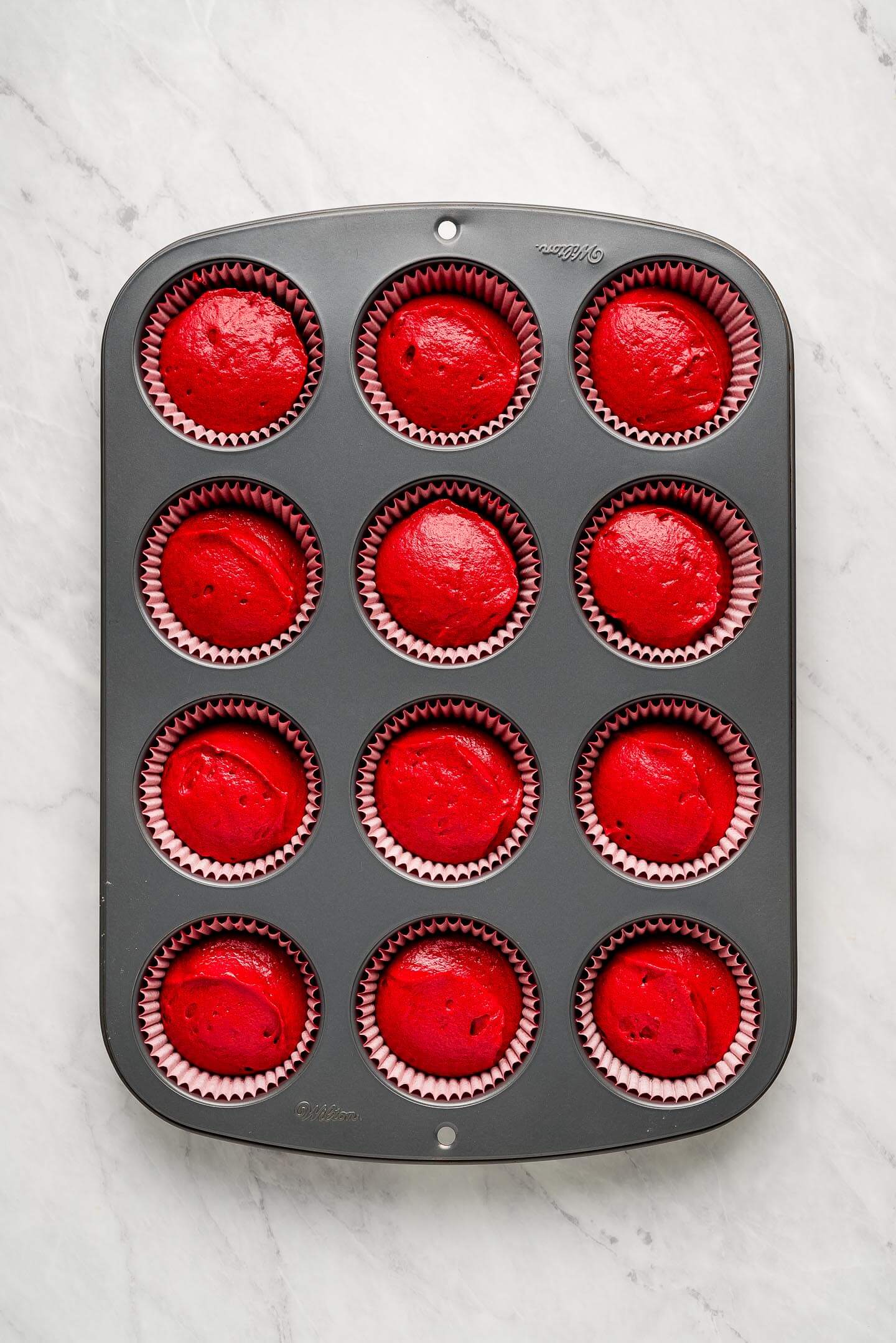 Red batter in a cupcake tin with paper liners.