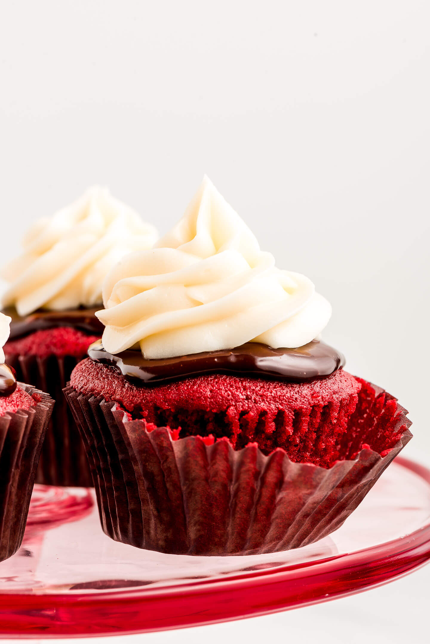 Close up of a Red Velvet cupcake topped with ganache and cream cheese frosting on a pink platter.