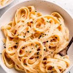 A bowl of Authentic Fettuccine Alfredo garnished with Parmesan and parsley.