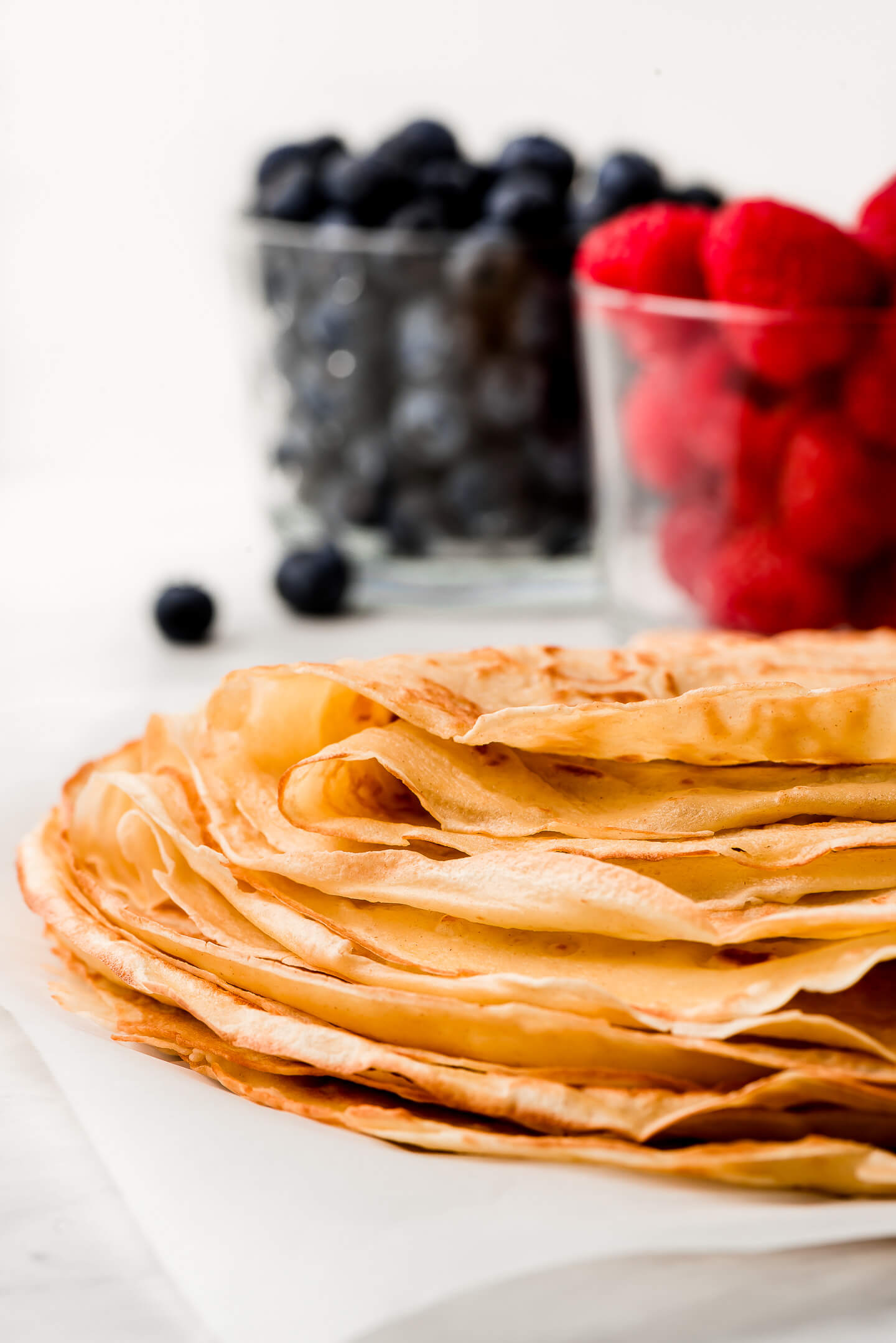Crepes stacked on top of each other and bowls of berries.