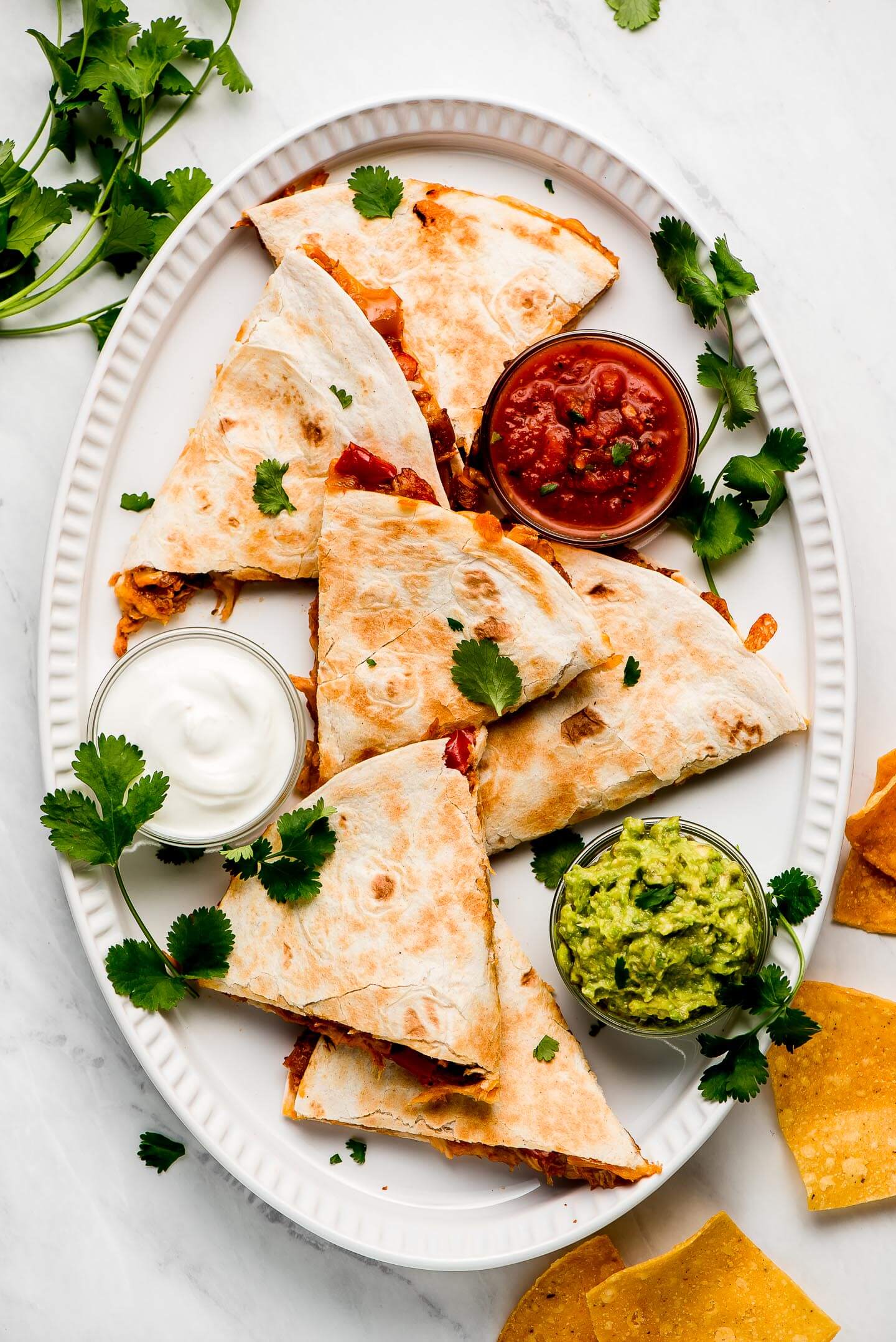 Triangles of quesadillas on a large platter with salsa, sour cream, and guacamole.