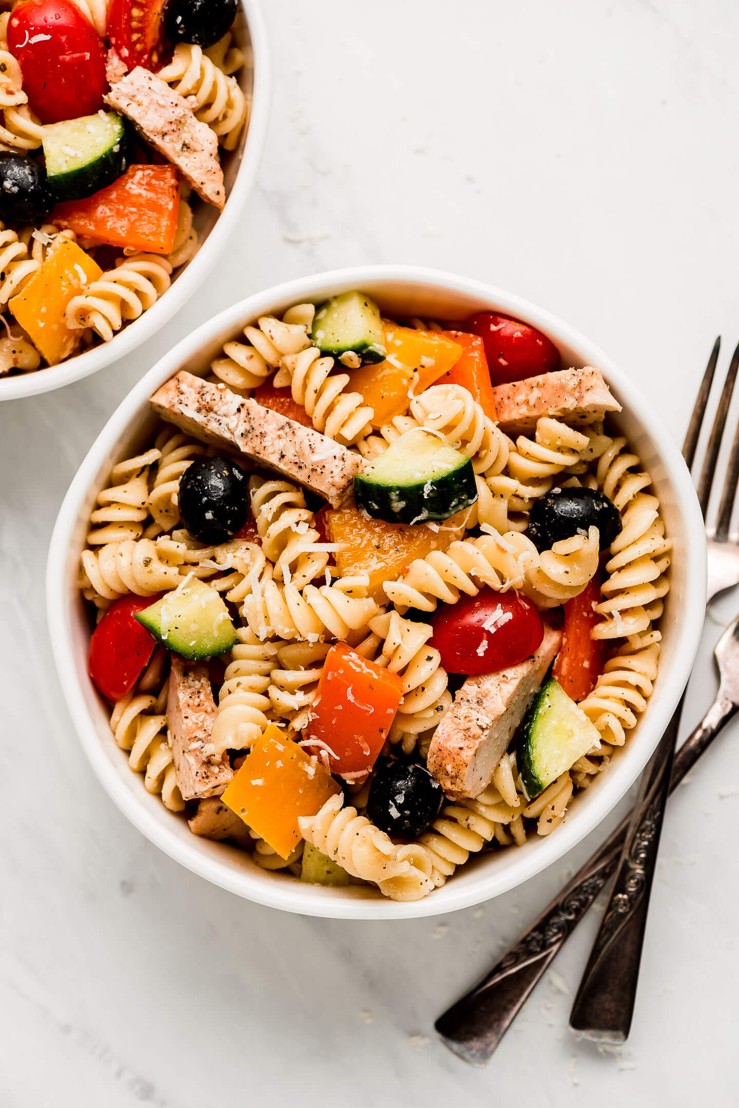 Two bowls of pasta salad with grilled chicken and vegetables.