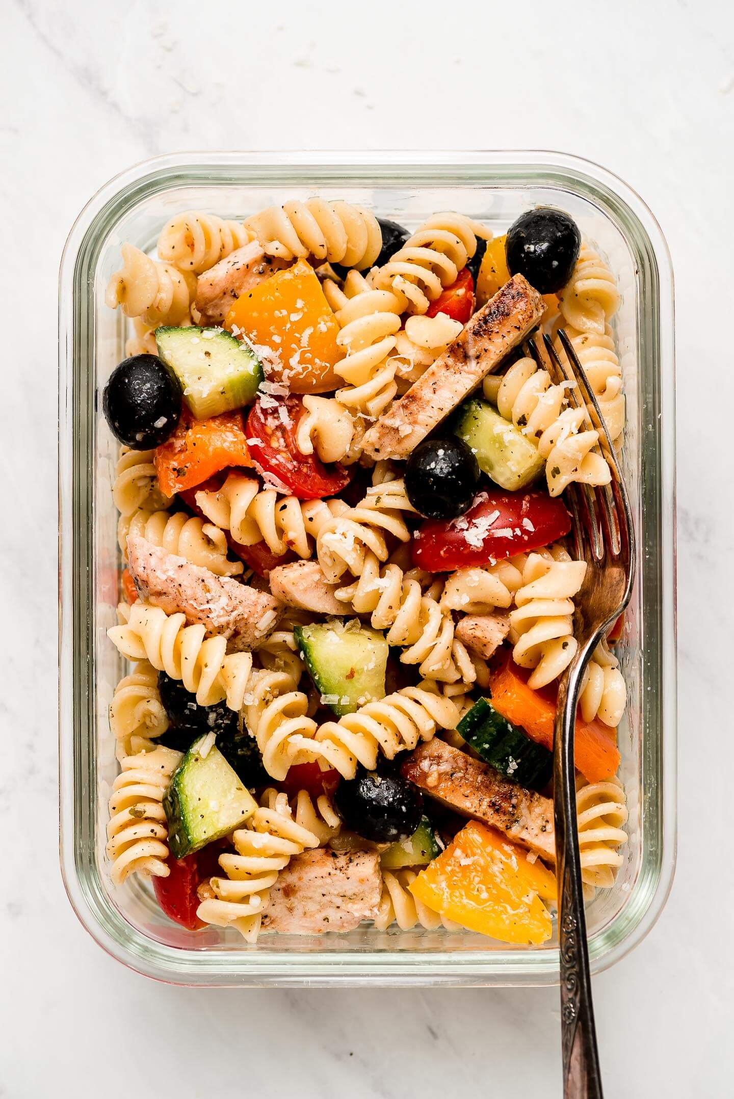 Pasta salad with chicken and vegetables in a glass meal prep container.