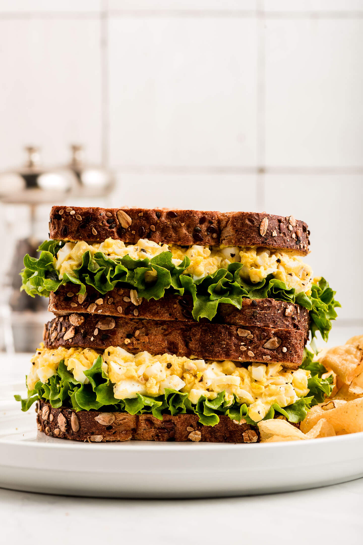 Two Egg Salad Sandwiches stacked on top of each other on a plate.