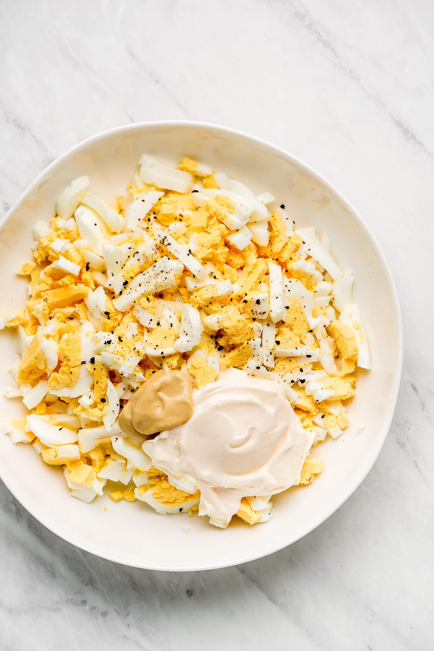 A bowl of chopped hard boiled eggs, mayonnaise, mustard, and salt & pepper.