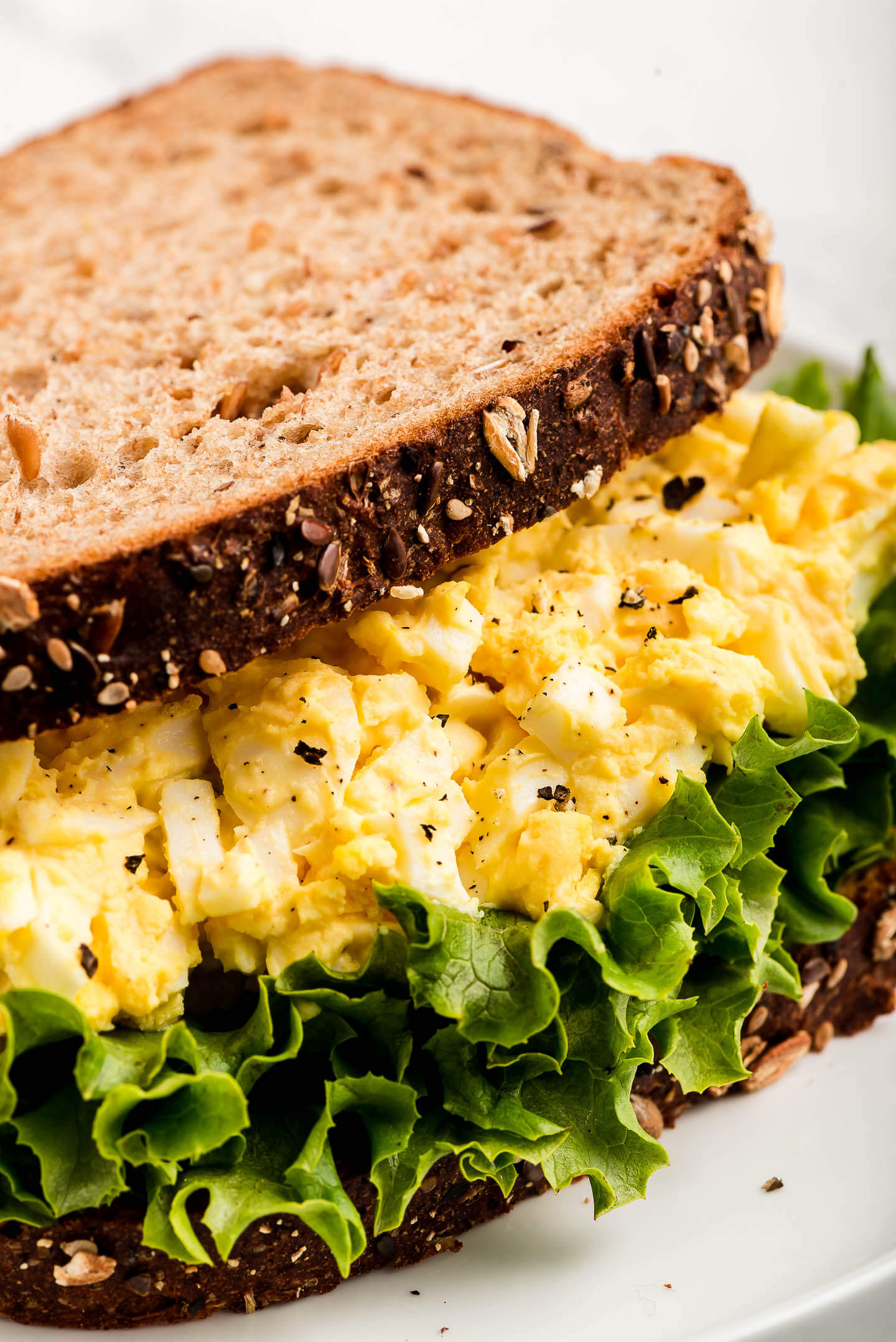Egg salad on lettuce between two slices of whole grain bread.