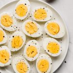 Hard boiled eggs cut in half on a plate sprinkled with salt and pepper.