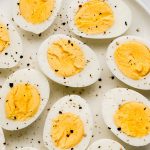Hard boiled eggs cut in half on a plate sprinkled with salt and pepper.