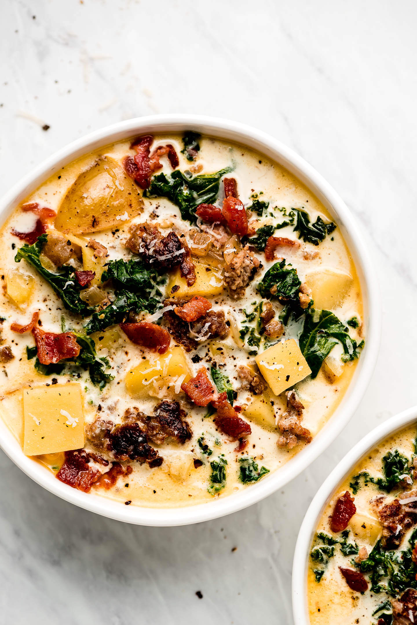 Two bowls of soup with sausage, potatoes, kale, and bacon.