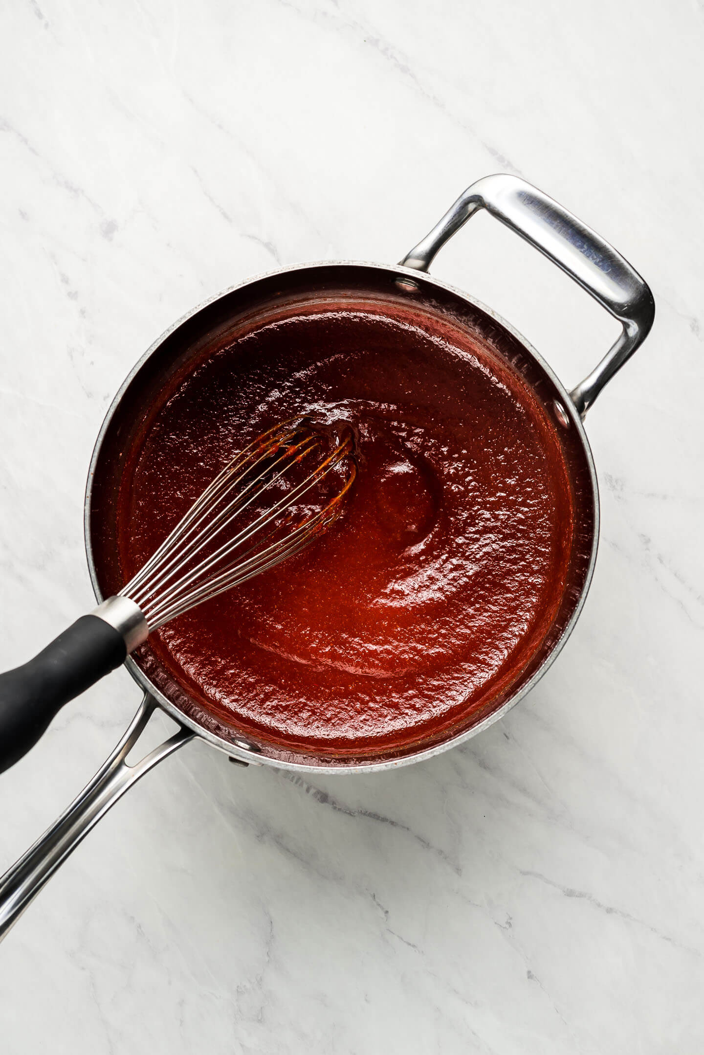A pot of homemade barbecue sauce with a whisk.