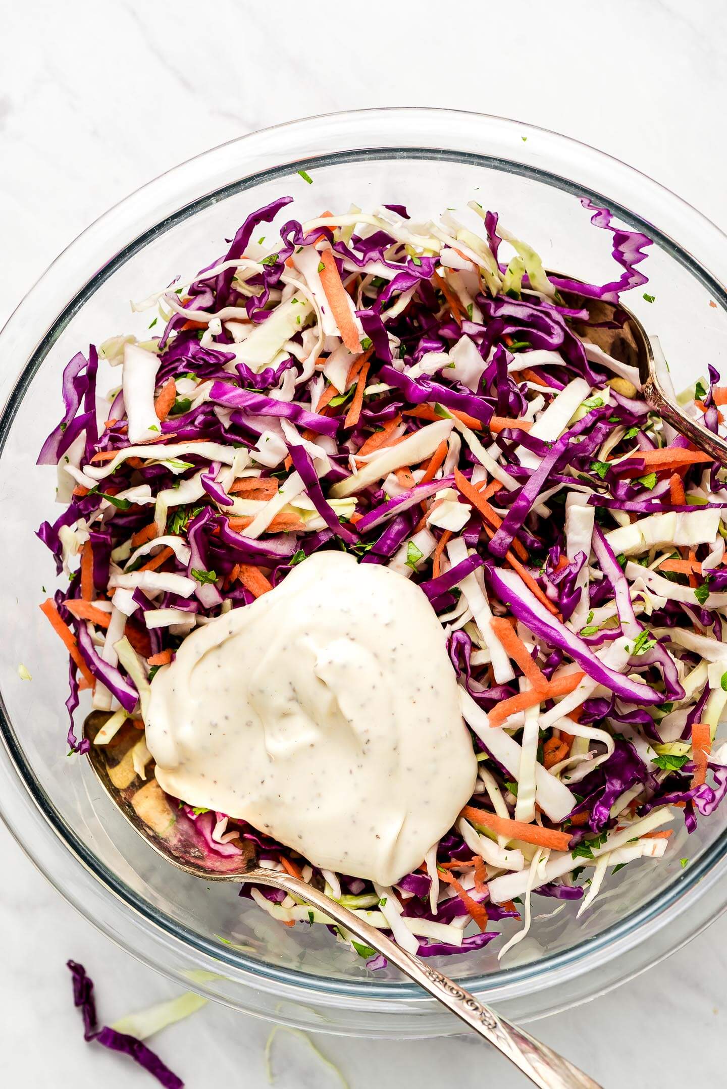 A bowl of shredded cabbage and carrots with a glob of dressing on top.