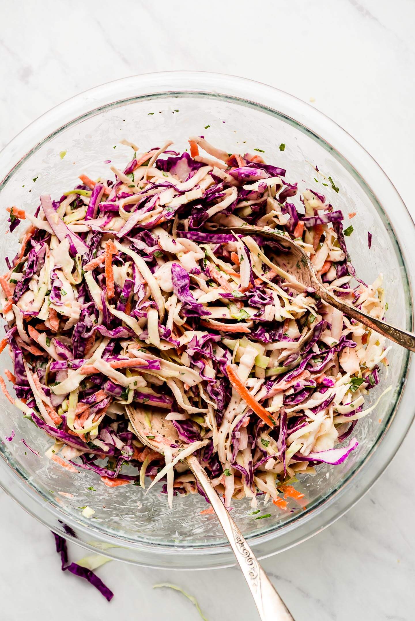 A glass mixing bowl of Coleslaw with two serving spoons.
