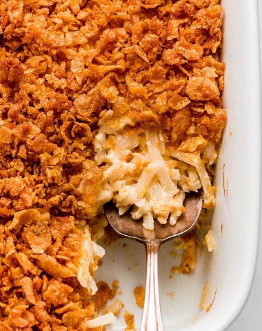 Close up of Funeral Potato Casserole in a pan with a serving spoon.