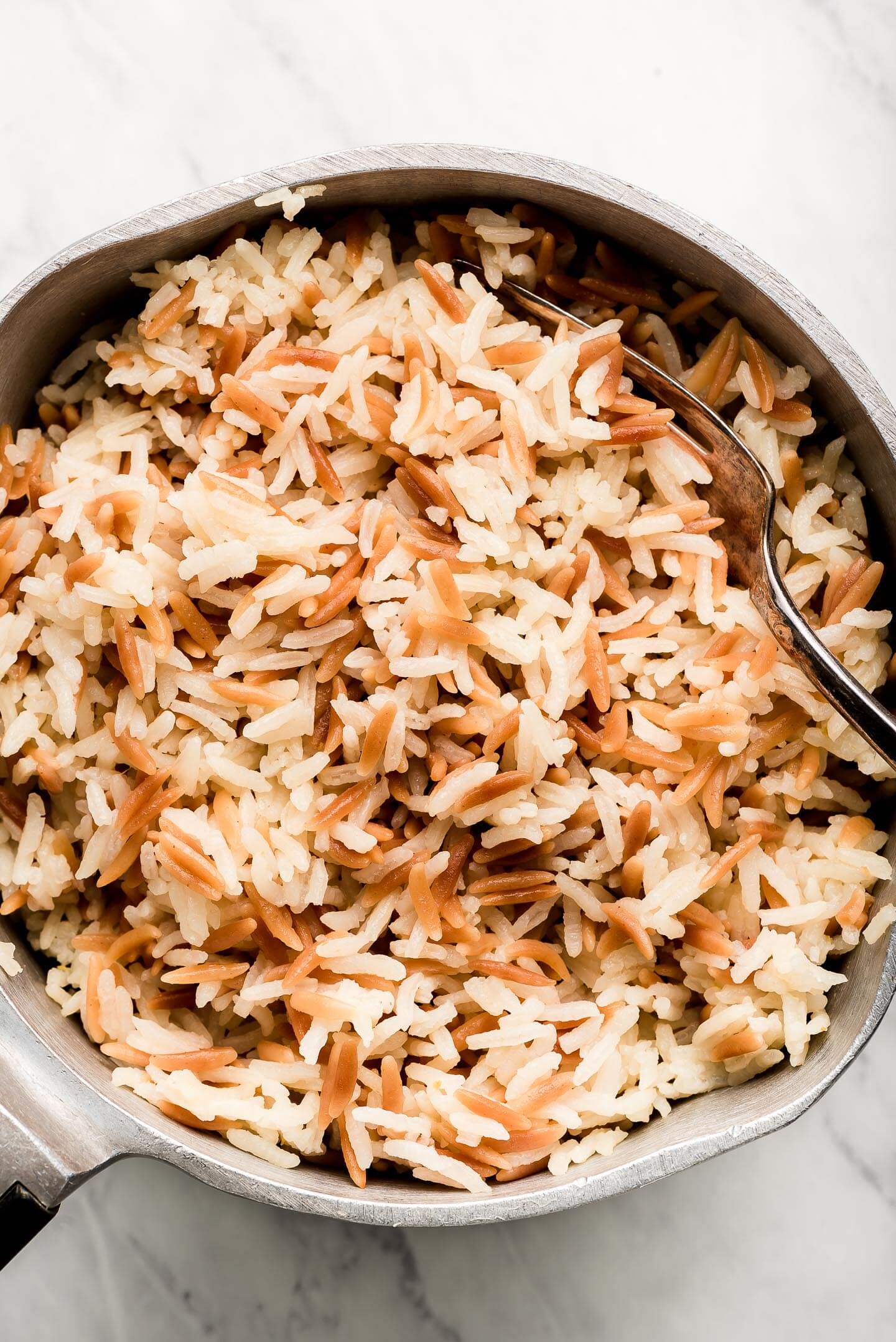 A pot of fluffed Orzo Rice with a fork in the side.