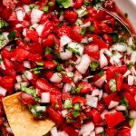 Pico de Gallo in a white serving bowl with tortilla chips around it.