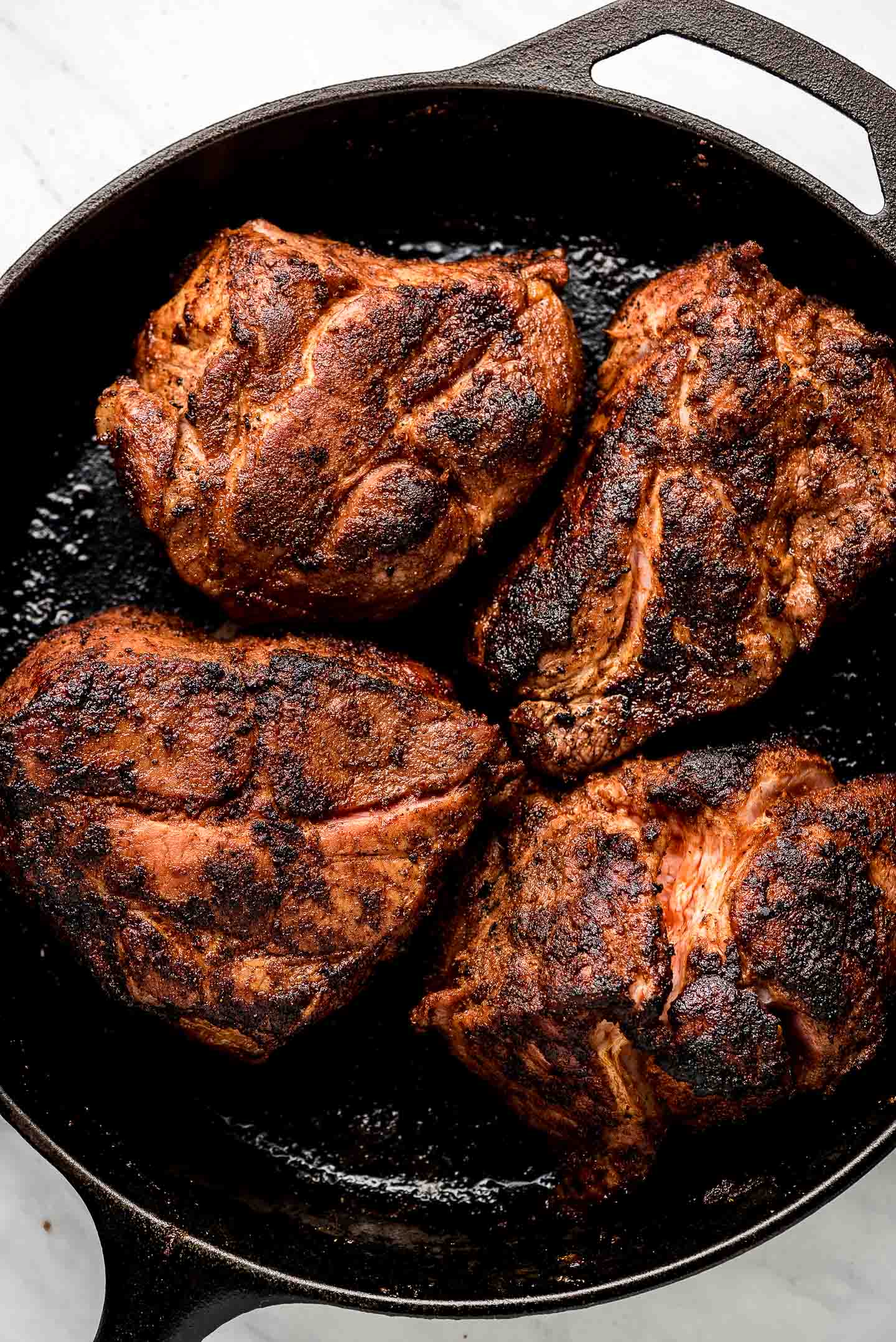 Browned cuts of pork shoulder in a a cast iron pan.