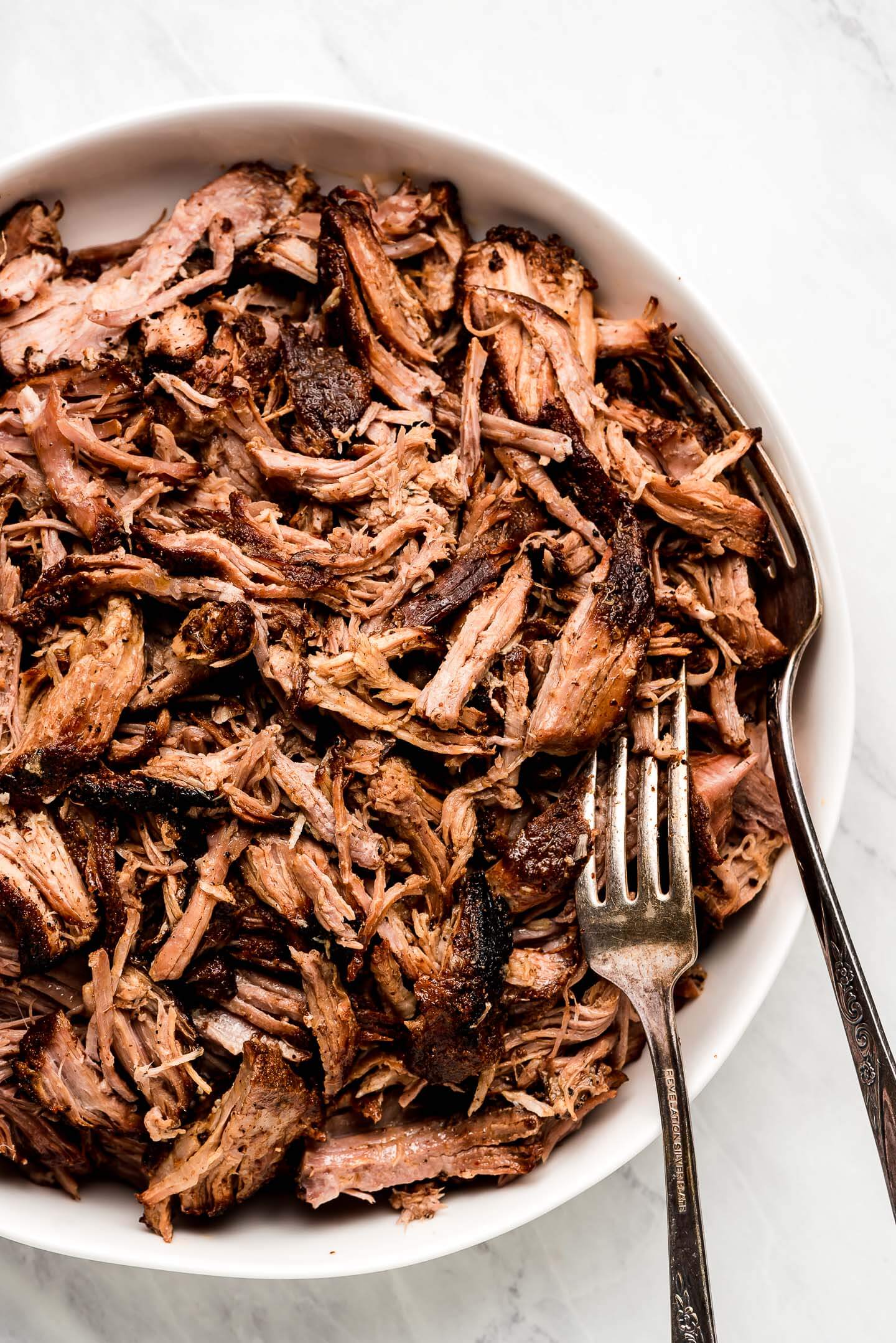 Pulled pork in a white serving bowl and forks in the side.