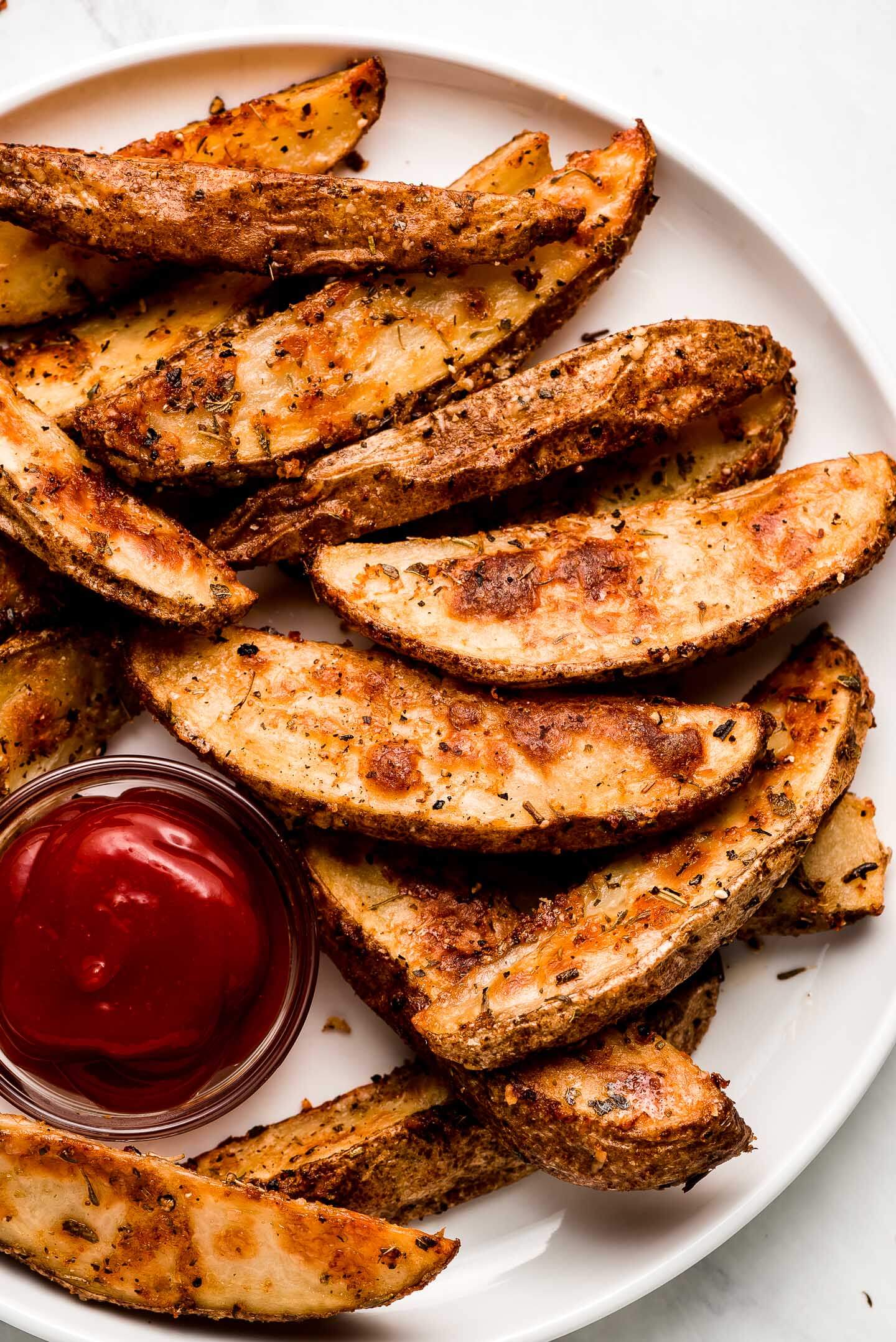 Close up of crispy Baked Potato Wedges on a plate with ketchup.