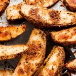A spatula lifting Potato Wedges off of of baking sheet.