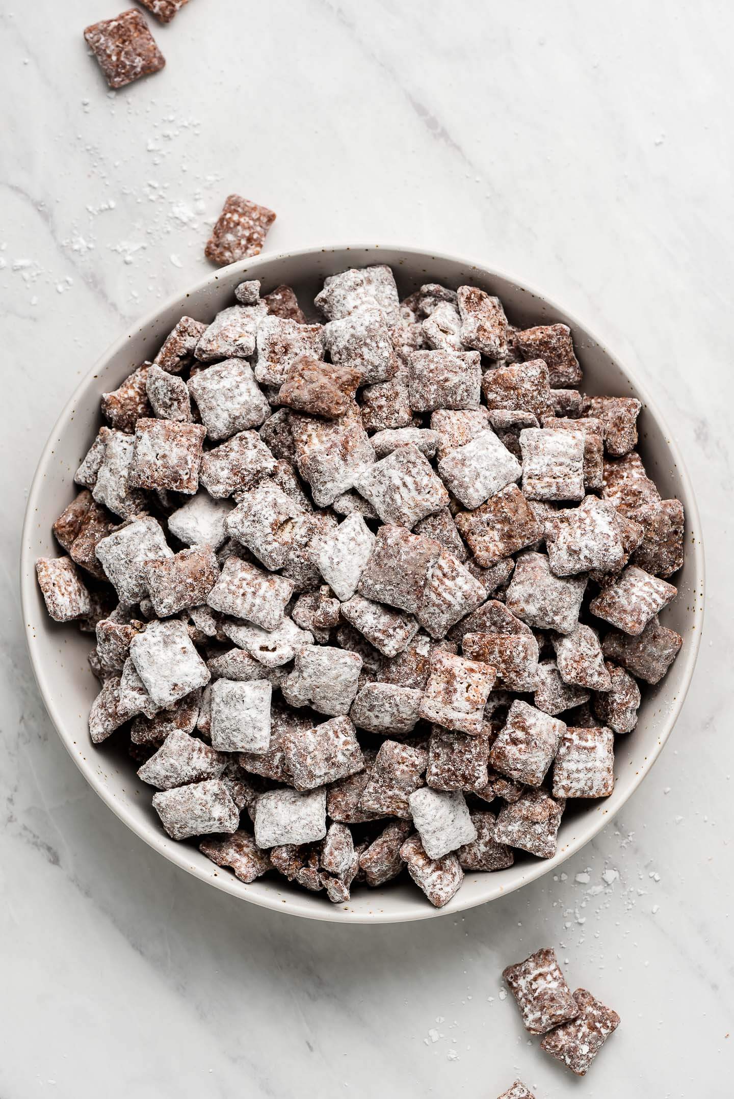 A white bowl of Muddy Buddies with a few on surface around bowl.