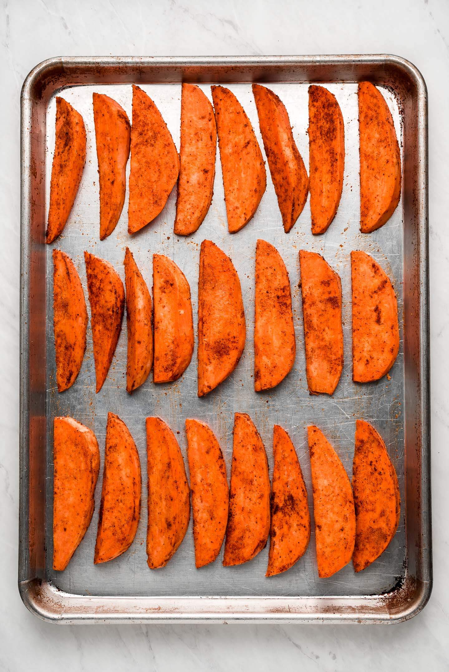 Raw sliced sweet potatoes lined up on a baking sheet.