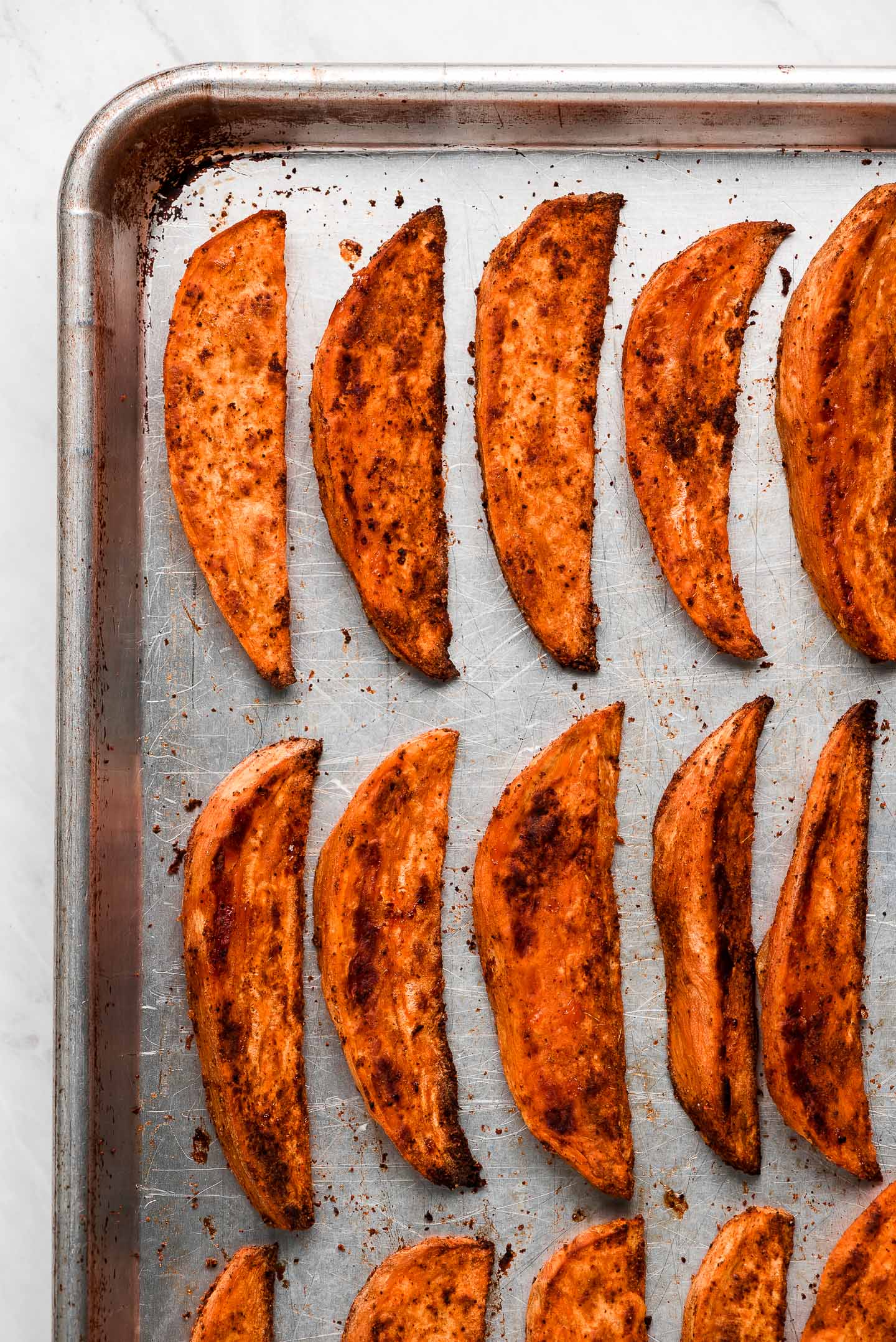 Baked Sweet Potato Wedges lined up on a baking sheet.