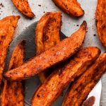 Baked Sweet Potato Wedges lifted up with spatula from a pan.