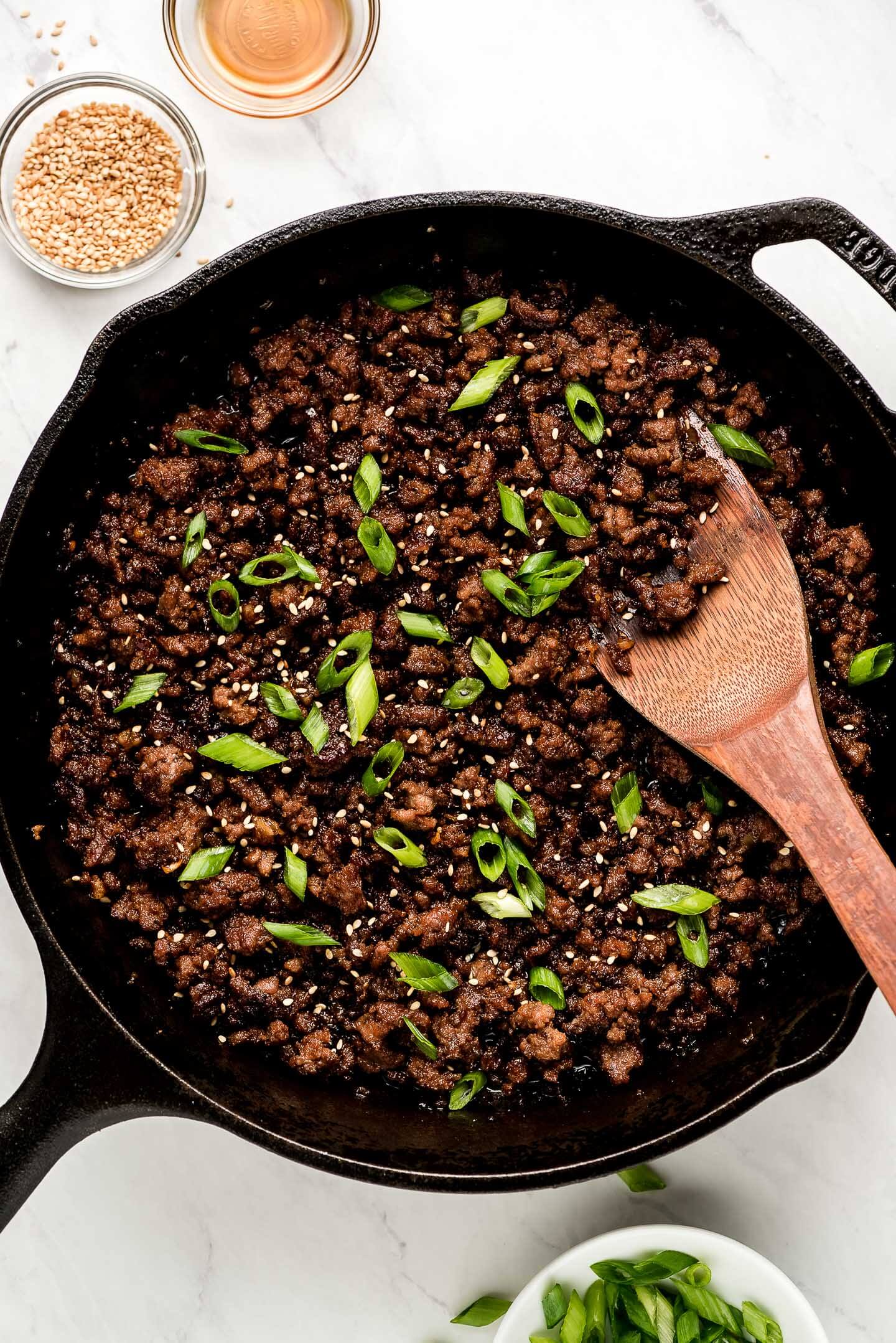 Skillet of Korean Ground Beef garnished with green onions, sesame seeds, and oil.