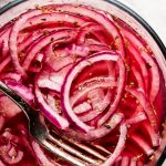 Glass bowl with Mexican Pickled Onions with containers of oregano, salt, and limes around.