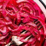 A glass bowl with marinated pink Mexican Pickled Onions with a squeezed lime to the side.